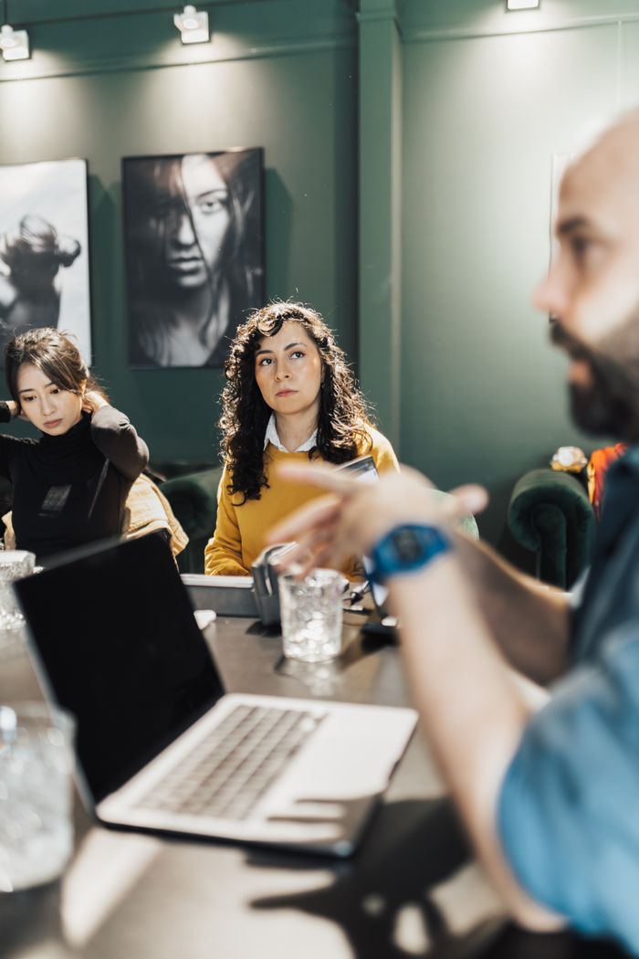 Professionals discussing projects around a conference table with laptops and notepads in an office.